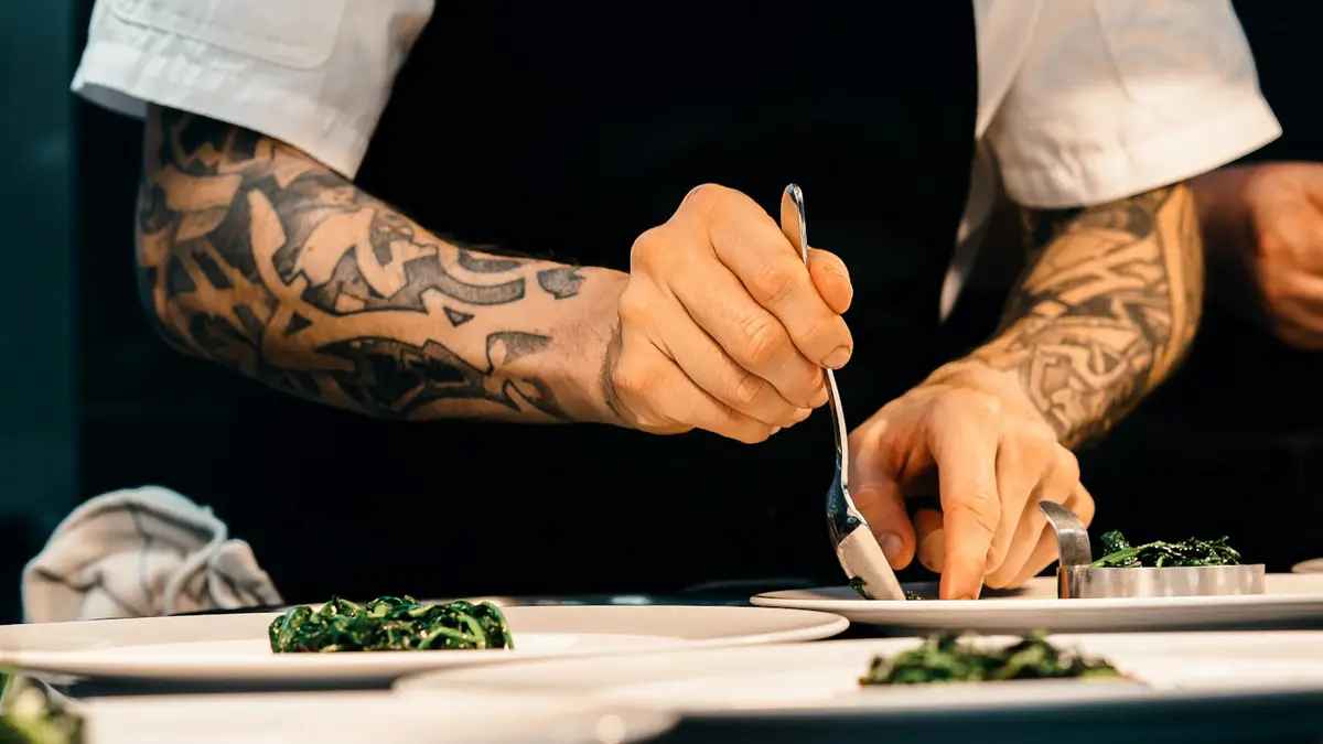 A chef's hands plating a dish with a spoon
