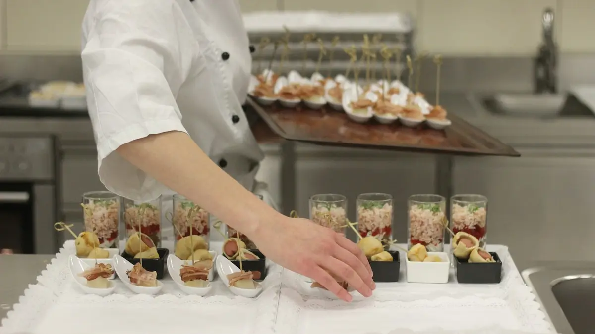 A chef in whites arranging small plates of food on a counter